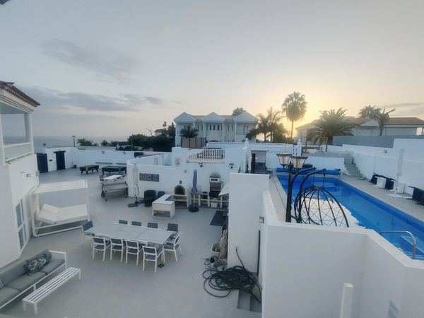 Wide sunset view of the outdoor area: canopy daybed, dining table, pool and sea on the horizon