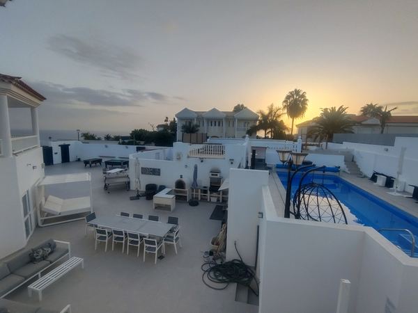 Sunset between the palm trees over the terrace and private pool, with the sea on the horizon